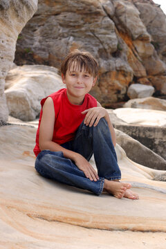 A happy young boy dressed in denim jeans and tank top, relaxing on some sandstone  rocks