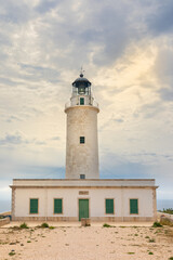 Fototapeta na wymiar Lighthouse of La Mola, on the island of Formentera. Vertical photo on a cloudy day, with a clearing that lets in the sun's rays. Balearic Islands, Spain.