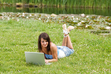 cute brunette in casual dress standing alone on the grass and working on the computer