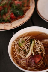 pho broth, Vietnamese soup in a deep plate with meat, wooden Chinese sticks and two quail eggs on a dark background