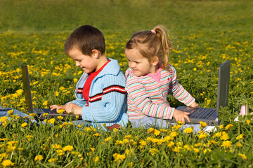 Happy kids with laptops on the spring flower field