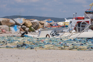 Many fishing nets and floats, stacked on a quayside with fish boat background. Selective focus.