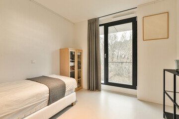 a bedroom with a bed, desk and large window looking out onto the trees in the photo is taken from inside