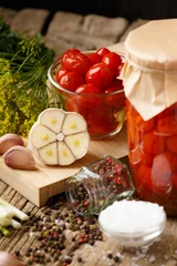 Gordijnen Canned cherry tomatoes in a jar and a bowl, spices and herbs on a wooden background. © Наталья Марная