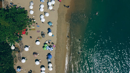Fototapeta na wymiar Turistas e guarda sóis na praia da feiticeira em Ilhabela captada do alto por um drone. 
