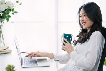 Asian woman working on laptop computer at home relaxing and chilling happily.