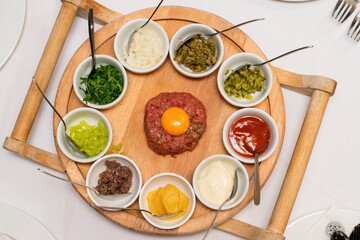 Restaurant waiter serving elaborate  - Beef tartare served on wooden board with various garnishes and egg yolk and person eats it