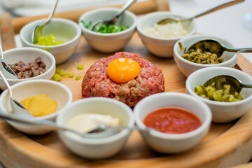 Restaurant waiter serving elaborate  - Beef tartare served on wooden board with various garnishes and egg yolk and person eats it