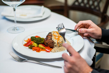 Delicious beef cutlet with grill vegetables on white plate. man cut and eat meat. men's hands holding knife and fork cutting steak