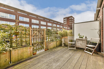 an outside area with wooden decking and plants on the side of the building in the background is a blue sky filled with white