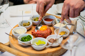 Restaurant waiter serving elaborate  - Beef tartare served on wooden board with various garnishes and egg yolk and person eats it