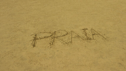 Palavra Praia escrito na areia de uma praia brasileira. 