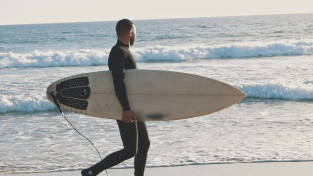 A man walking along the shore with a large surfboard