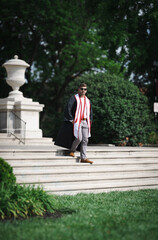 Fototapeta premium University of Louisville male graduate walking down the stairs of one of the campus buildings wearing a gown and honor ropes