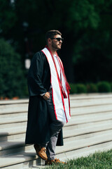 Wearing a graduation gown and honor ropes, a newly graduated college student stands confidently on a staircase, gazing ahead.