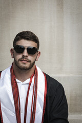 Obraz premium Close up portrait of University of Louisville male graduate wearing sunglasses, gown and honors ropes in front of white stone background