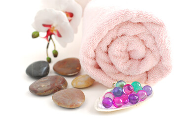 Obraz na płótnie Canvas Pink rolled up towel with a stack of massage stones and bath beads on white background