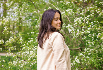 beautiful woman girl outside in park through blossom tree branches white small flowers.natural beauty no makeup female smiling holding flowers in palms.outdoor shooting spring time easter.brunette hai