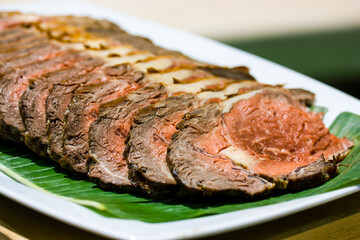 A plate with veal meat cut served on a green leaf on a white plate with appetizer. Sliced baked meat on a kitchen table. Portion of delicious rare roast beef sirloin of fillet, steak. Seared chicken.