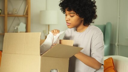 African girl unpacking delivery looking in box. Happy woman opening carton box. Female getting parcel looking at delivered goods items. Satisfied client positive feedback quick express deliver