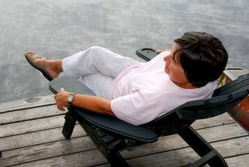 Fototapeta na wymiar Mature woman relaxing on a pier in a wooden chair