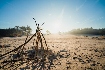 Natural children's hut built with sticks on sand with rising morning sun