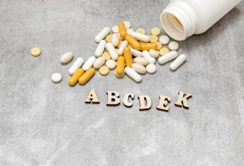 many pills tablets plastic blisters scatered from bottle.vitamins a b c d e and k.wooden letters forming word vitamins.medical concept, treatment,take medicine,antibiotics,food suplements.capsules