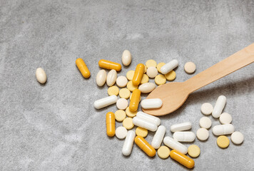different pills tablets capsules scattered on gray tiles background or in eco wood spoon or plastic one.woman take one oval pill with sushi sticks.treat illness,drug addictions,vitamins antibiotics