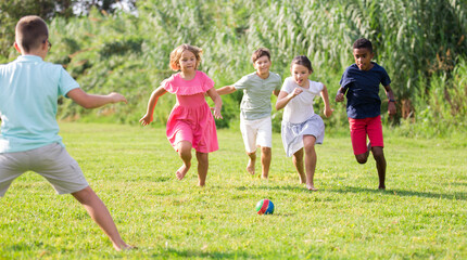 Obraz na płótnie Canvas International group of active tweenagers having fun together outdoors, playing football on green grass in summertime