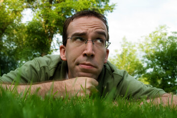 A young man lying in the grass and thinking outside