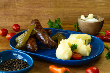 Grilled sausages with mashed potatoes and pickles on wooden background