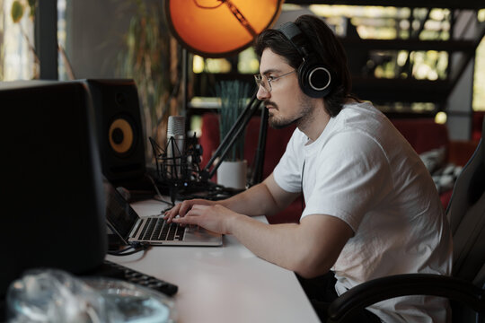 Concentrated Young Bearded Male Musician In Headphones Composing Music On Laptop During Workday In Recording Studio