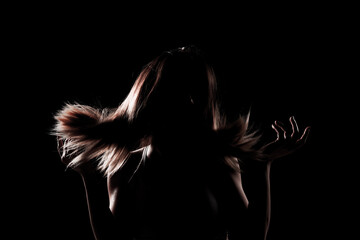 silhouette contour of a beautiful girl with blowing hair. Side lit studio portrait on dark...