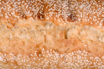 Crispy wheat flour baguette with sesame seeds on a wooden cutting board