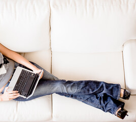 Cropped overhead view of woman reclining on white couch and using a laptop. Horizontal format.