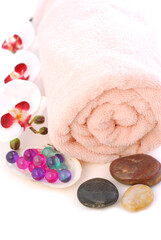 Obraz na płótnie Canvas Pink rolled up towel with massage stones and bath beads on white background