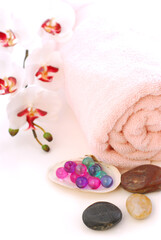Obraz na płótnie Canvas Pink rolled up towel with massage stones and bath beads on white background