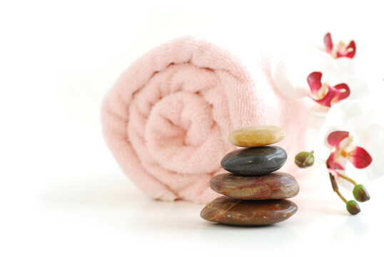 Pink rolled up towel with a stack of massage stones and orchid on white background