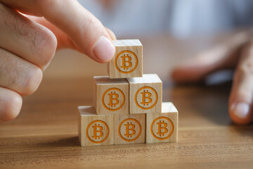 Businessman stacking wooden blocks on top of each other, wooden blocks have bitcoin symbols on them.