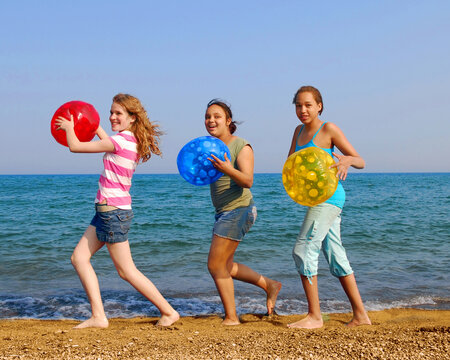 Three girls with colorful beach balls walking on sea shore