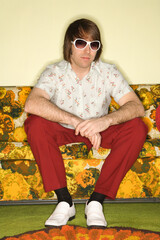 Portrait of Caucasian mid-adult man wearing sunglasses sitting on colorful retro sofa.