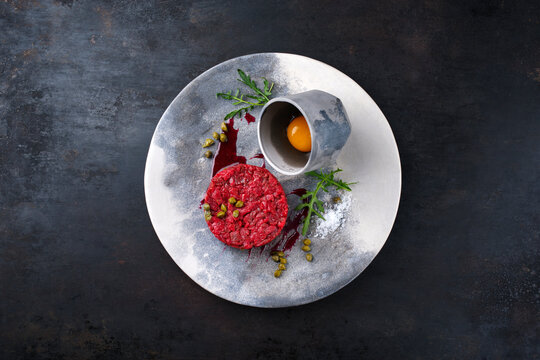 Gourmet Tartar roh aus Rinderfilet mit Ei, Rucola und Kapern serviert als Draufsicht auf einem Design Teller mit Textfreiraum