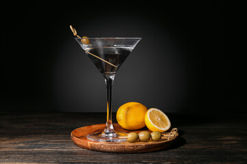Glass of tasty martini, lemons and olives on wooden table against dark background