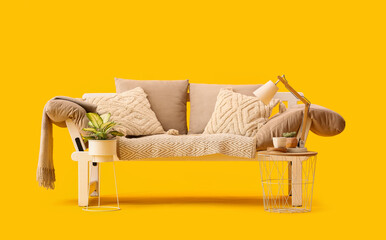 Cozy sofa with cushions, coffee table and houseplant on yellow background