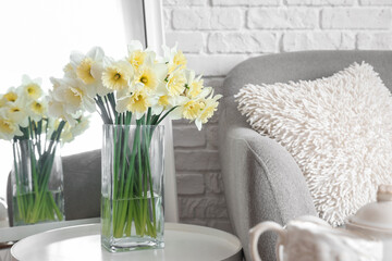 Vase with narcissus flowers on coffee table near mirror in interior of living room