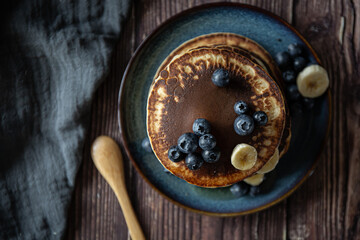 Pile of American pancakes with banana and blueberries on dark background 
