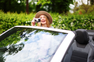leisure, road trip, travel concept - happy girl driving in cabriolet car and taking picture by film...