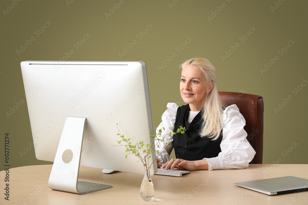 Poster mature female programmer working with computer at table on green background