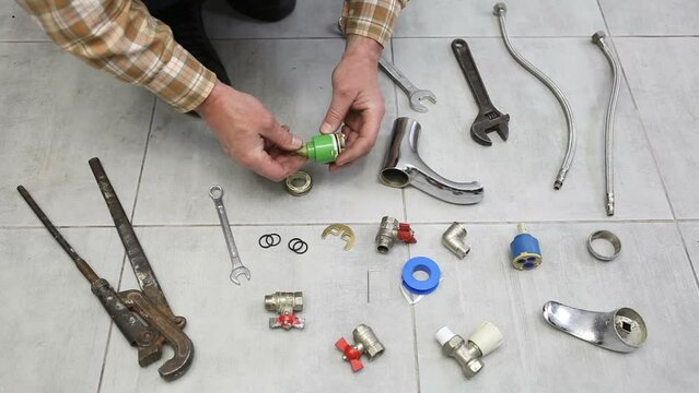 A wrench and a disassembled faucet lie on the floor in the kitchen. A man changes the cartridge and gaskets in the faucet.