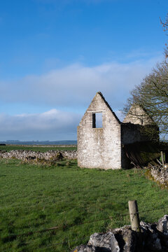 Old ruined, roofless barn sits in grassy field. Bright blue sky and cumulus clouds provides contrast to this limestone building.